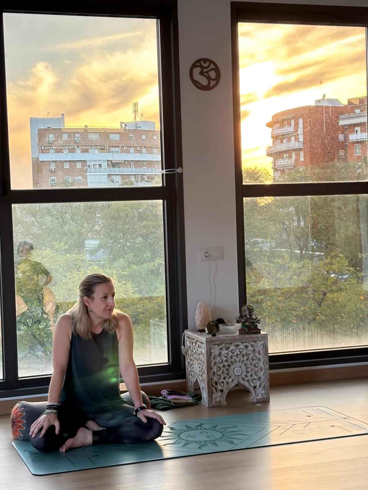 Belén, fundadora de MYBEYOGA, sentada sobre su esterilla junto a los ventanales de la sala al atardecer