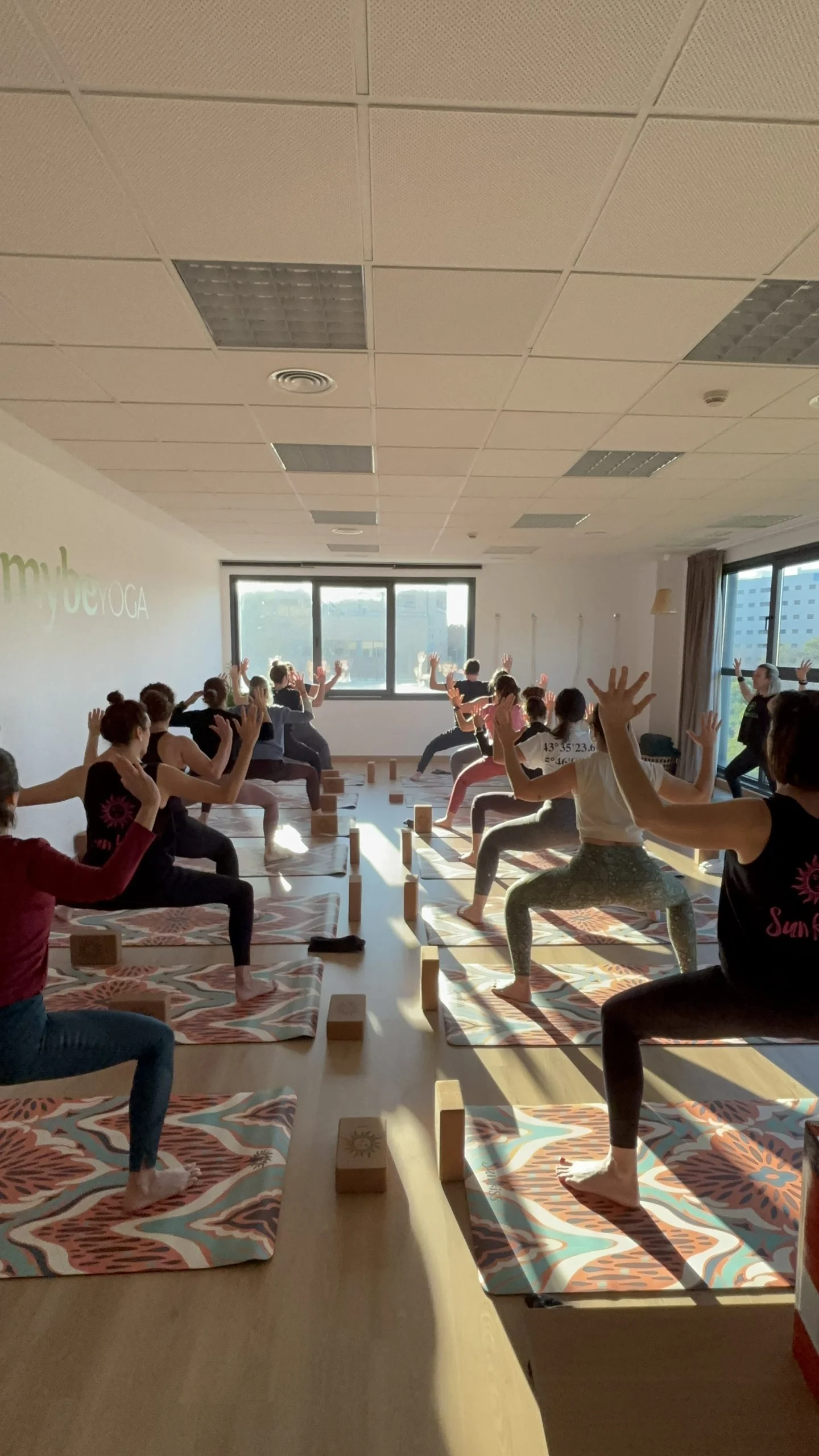 Grupo de alumnas practicando la postura del guerrero durante una clase en la sala de Mybeyoga