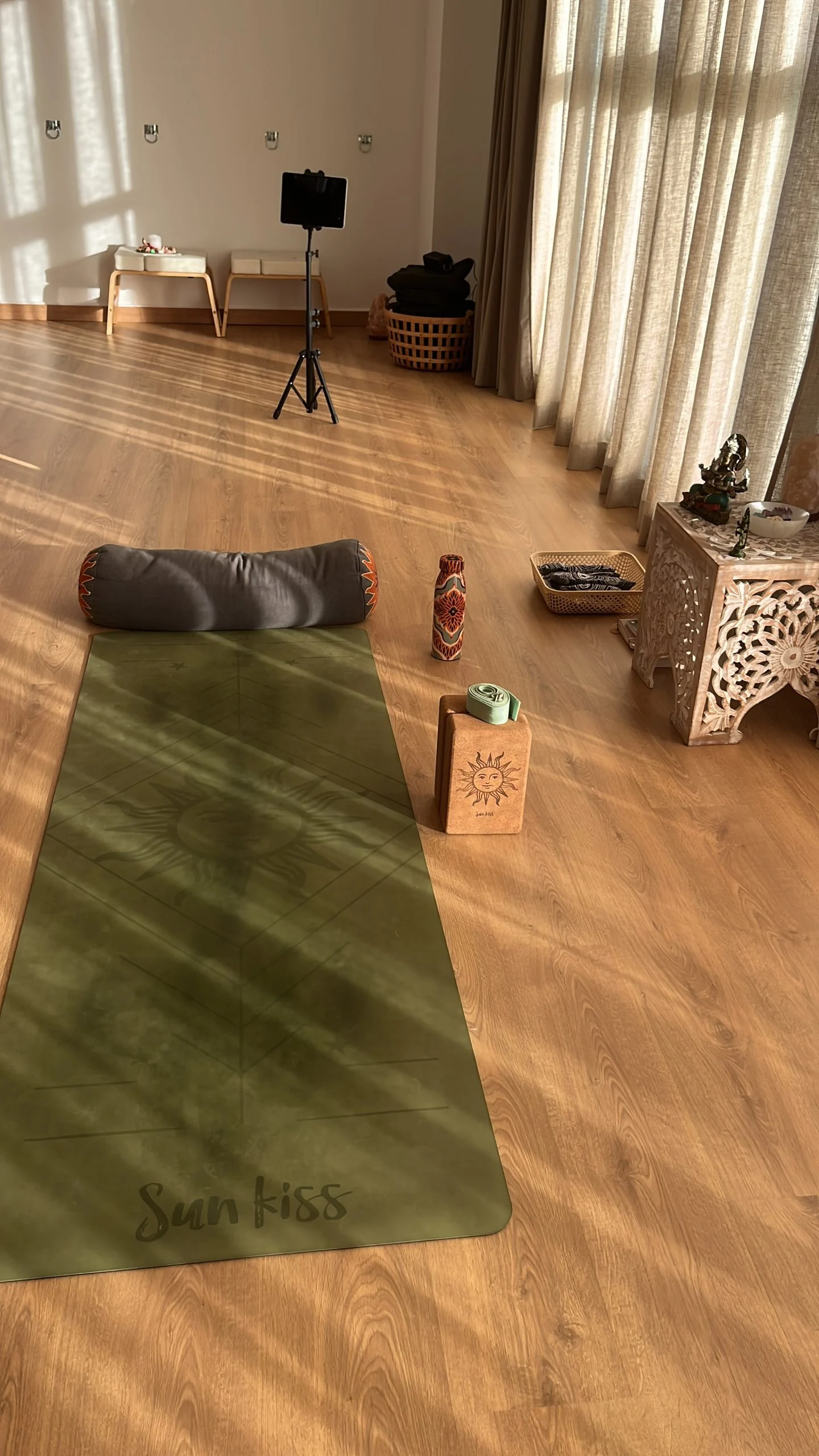 Esterilla verde con un cojín alargado y un bloque de corcho, preparada en la sala iluminada por el sol